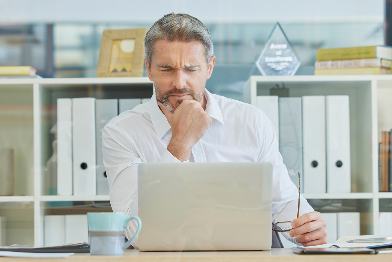 Muž v košili sedící v kanceláři zamyšleně sleduje obrazovku svého notebooku