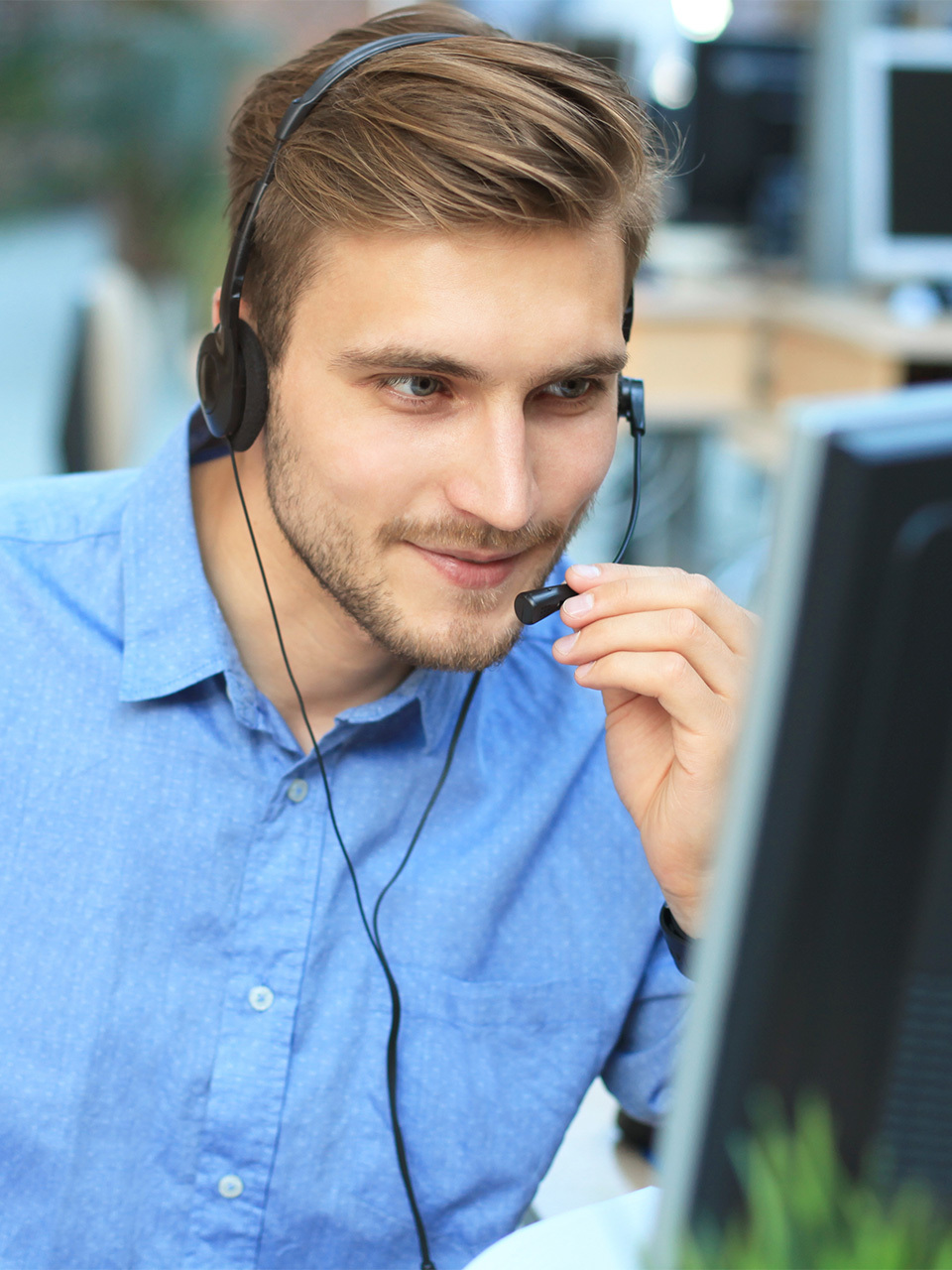 Muž v košili se sluchátky s mikrofonem pracuje na PC